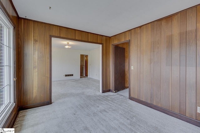 carpeted spare room featuring wood walls, visible vents, and ornamental molding