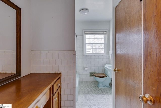 bathroom featuring toilet, a wainscoted wall, tile walls, and tile patterned floors