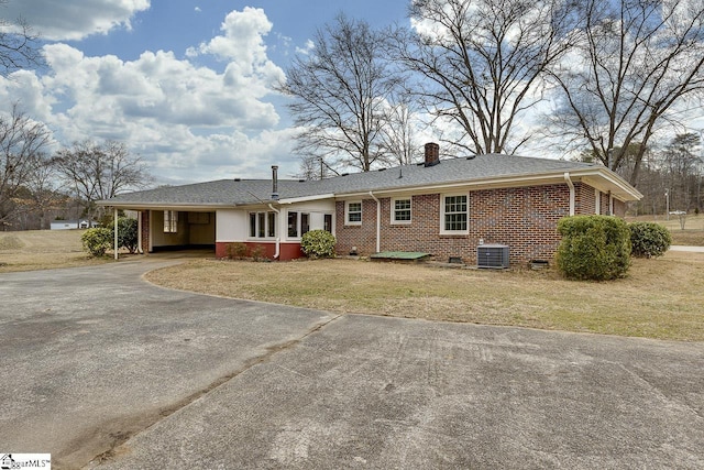 exterior space with brick siding, a chimney, central AC unit, a carport, and driveway