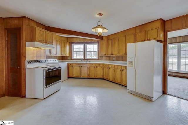 kitchen featuring light countertops, wood walls, a sink, white appliances, and under cabinet range hood