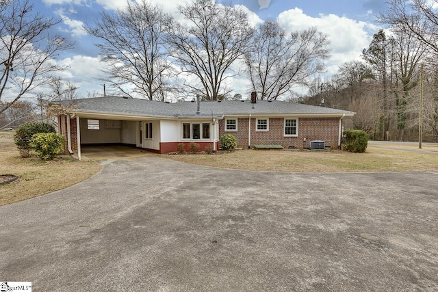 ranch-style home with driveway, brick siding, an attached carport, central air condition unit, and a front yard