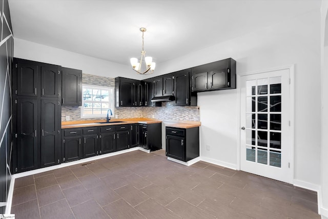 kitchen with tasteful backsplash, an inviting chandelier, a sink, and dark cabinets