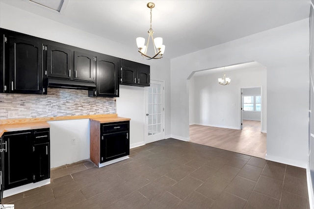 kitchen featuring dark cabinets, a notable chandelier, hanging light fixtures, and tasteful backsplash