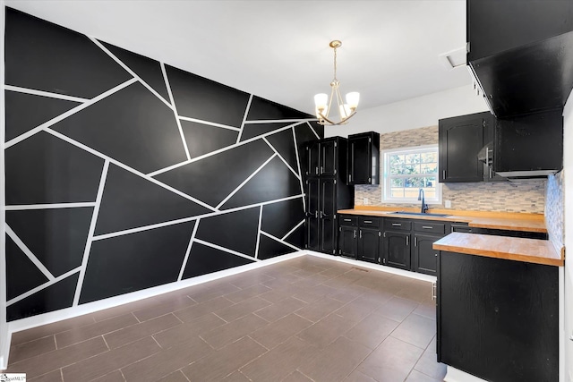 kitchen featuring decorative backsplash, wood counters, dark cabinetry, a chandelier, and a sink