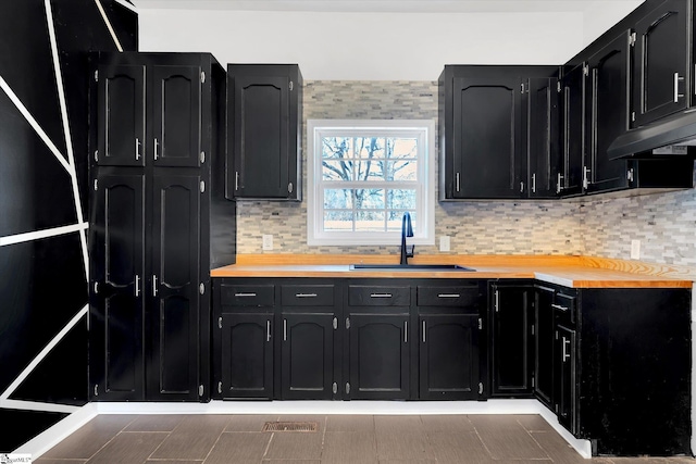 kitchen featuring under cabinet range hood, dark cabinetry, light countertops, and a sink