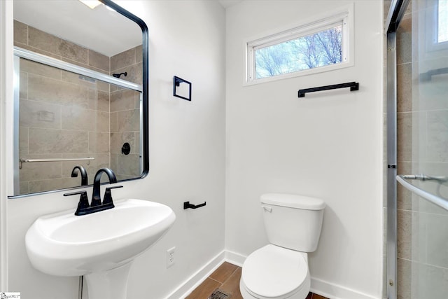 bathroom with baseboards, a tile shower, toilet, and wood finished floors