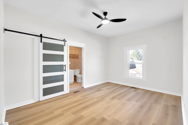 spare room with light wood finished floors, visible vents, a barn door, ceiling fan, and baseboards