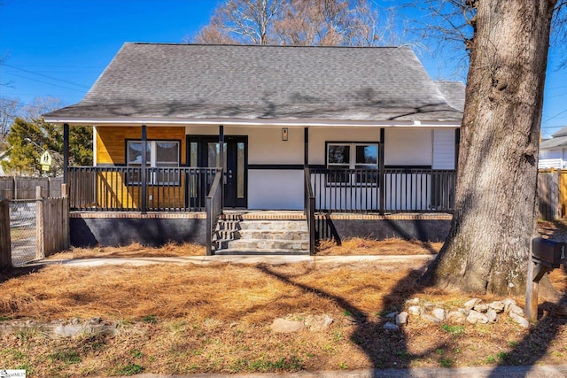 view of front facade featuring covered porch, roof with shingles, and fence