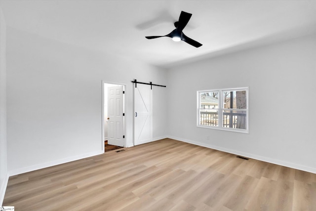 empty room with wood finished floors, ceiling fan, baseboards, and a barn door