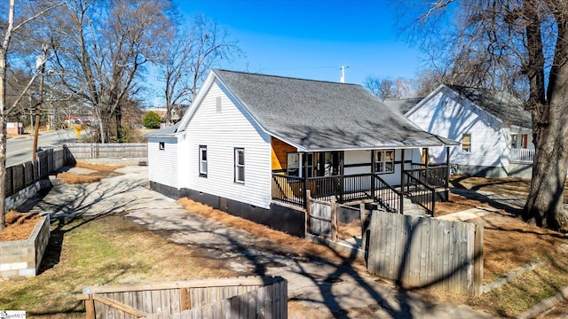 view of property exterior with a fenced front yard, a porch, a shingled roof, crawl space, and driveway