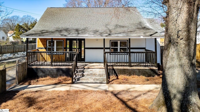 view of front of house featuring covered porch, a shingled roof, and fence