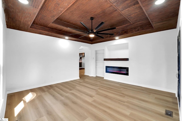 unfurnished living room featuring visible vents, built in features, a raised ceiling, a glass covered fireplace, and wooden ceiling