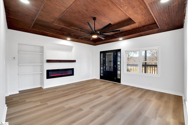 unfurnished living room with built in features, a raised ceiling, a glass covered fireplace, wooden ceiling, and wood finished floors