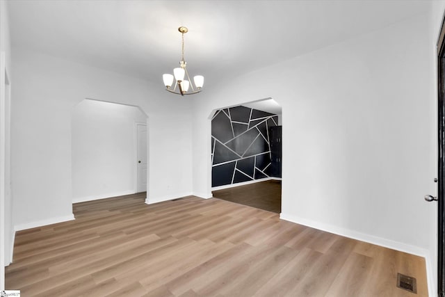 unfurnished dining area with baseboards, visible vents, arched walkways, light wood-style flooring, and a notable chandelier