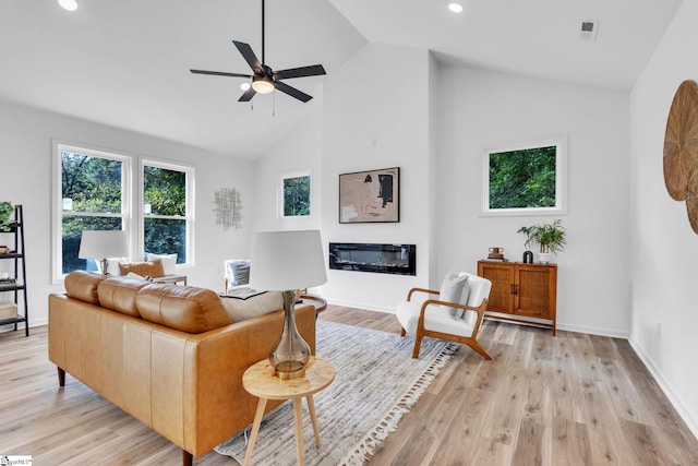 living area featuring ceiling fan, light wood finished floors, a glass covered fireplace, and baseboards