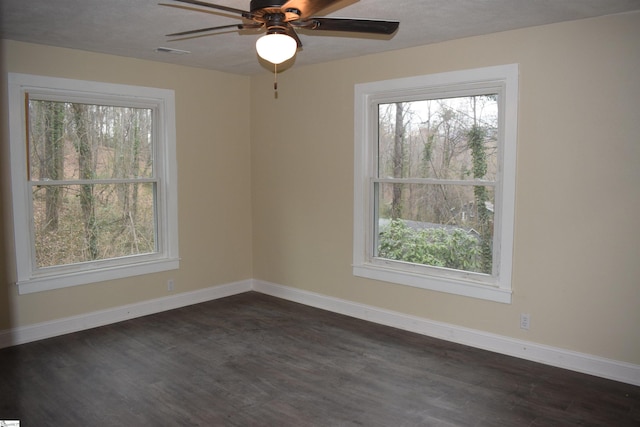 unfurnished room featuring visible vents, baseboards, dark wood-style flooring, and a wealth of natural light