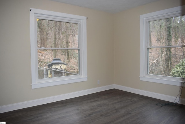 empty room featuring dark wood-style flooring, a wealth of natural light, and baseboards