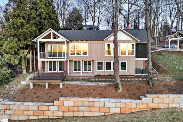 view of front facade with a balcony, a shingled roof, and central AC