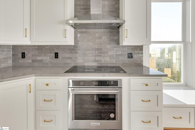 kitchen with black electric stovetop, wall chimney range hood, oven, and white cabinetry