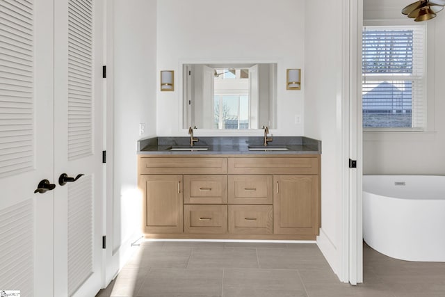 full bath featuring tile patterned floors, a freestanding tub, a sink, and double vanity