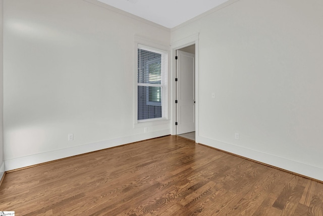 spare room with crown molding, wood finished floors, and baseboards