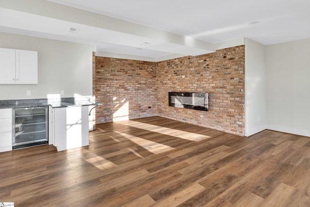 unfurnished living room featuring wine cooler, a brick fireplace, brick wall, wood finished floors, and baseboards