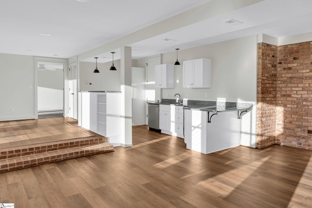 kitchen with a breakfast bar, wood finished floors, white cabinets, stainless steel dishwasher, and dark stone counters