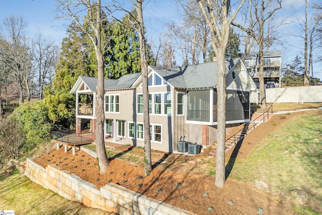 view of front of home with a shingled roof, a sunroom, stairs, central air condition unit, and a front lawn