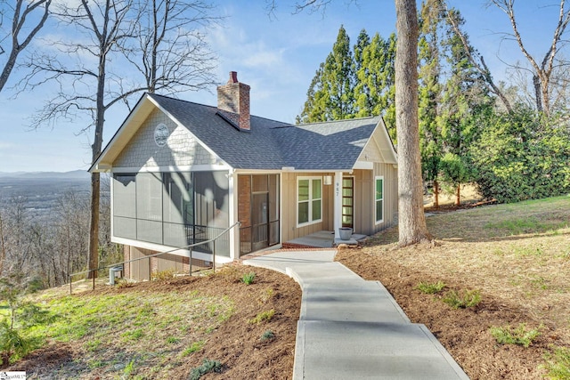 view of front of house with a sunroom, roof with shingles, and a chimney