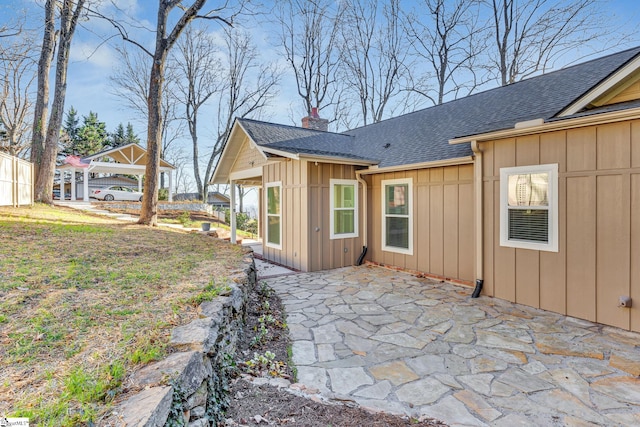 exterior space featuring a shingled roof, a patio, a chimney, and board and batten siding