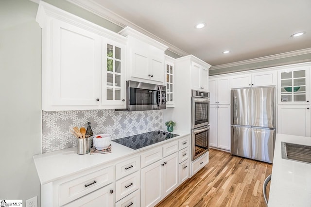 kitchen with white cabinets, light countertops, appliances with stainless steel finishes, light wood-type flooring, and backsplash