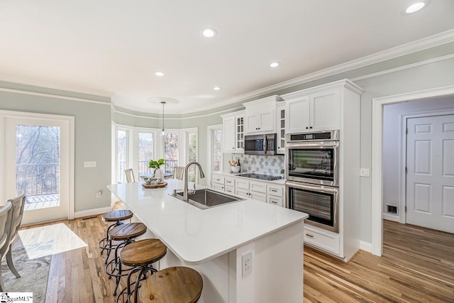 kitchen with stainless steel appliances, white cabinetry, a sink, light wood-type flooring, and a kitchen breakfast bar