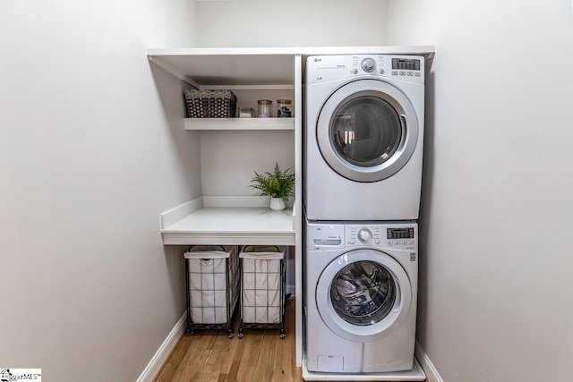 laundry area with laundry area, stacked washer / dryer, wood finished floors, and baseboards