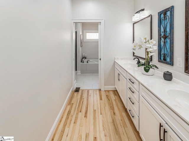 full bathroom featuring wood finished floors, a sink, baseboards, a bath, and double vanity