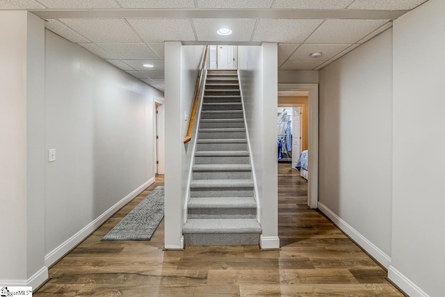 stairway with recessed lighting, wood finished floors, a paneled ceiling, and baseboards