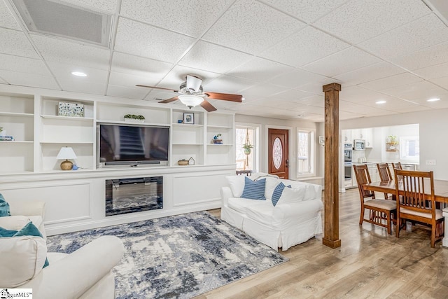 living room with decorative columns, visible vents, a ceiling fan, a glass covered fireplace, and light wood-type flooring