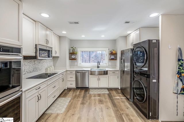 kitchen featuring appliances with stainless steel finishes, a sink, stacked washing maching and dryer, and open shelves