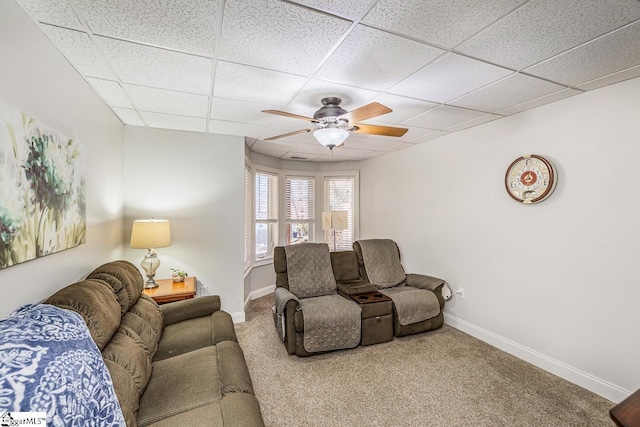 living room featuring carpet flooring, ceiling fan, a drop ceiling, and baseboards