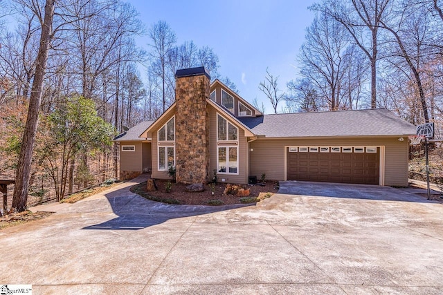 mid-century home featuring a garage, driveway, a shingled roof, and a chimney