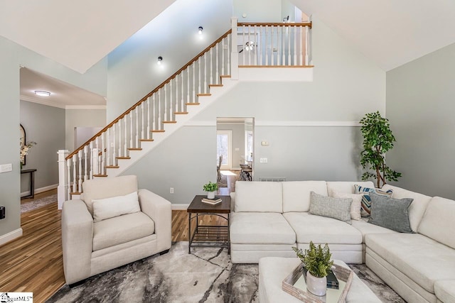 living room with baseboards, a towering ceiling, wood finished floors, stairs, and crown molding