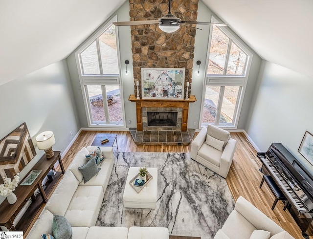 living room featuring a tiled fireplace, ceiling fan, wood finished floors, high vaulted ceiling, and baseboards