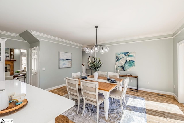 dining room with light wood-type flooring, baseboards, crown molding, and a tiled fireplace