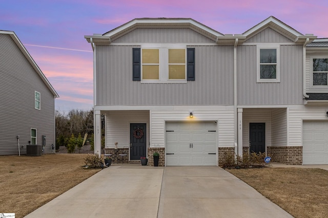 view of front of home with driveway, an attached garage, central AC, and brick siding