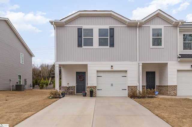 view of front of property with central AC unit, an attached garage, brick siding, driveway, and a front yard