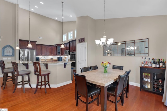 dining area with baseboards, wood finished floors, an inviting chandelier, high vaulted ceiling, and recessed lighting