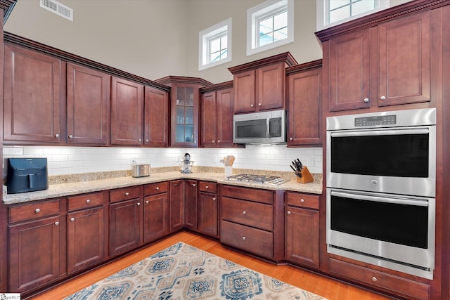 kitchen featuring tasteful backsplash, visible vents, a high ceiling, appliances with stainless steel finishes, and light stone countertops