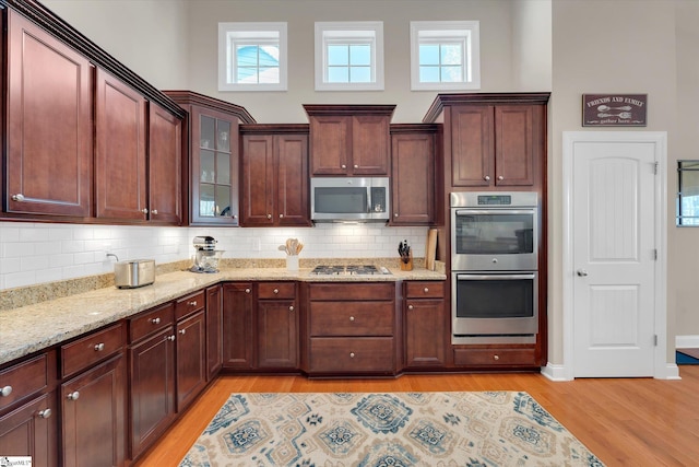 kitchen featuring stainless steel appliances, light wood-type flooring, glass insert cabinets, and light stone countertops