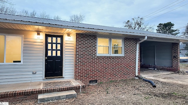 view of exterior entry with crawl space, brick siding, and metal roof