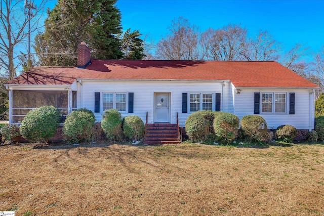 view of front of home with roof with shingles, a chimney, a front yard, and a sunroom