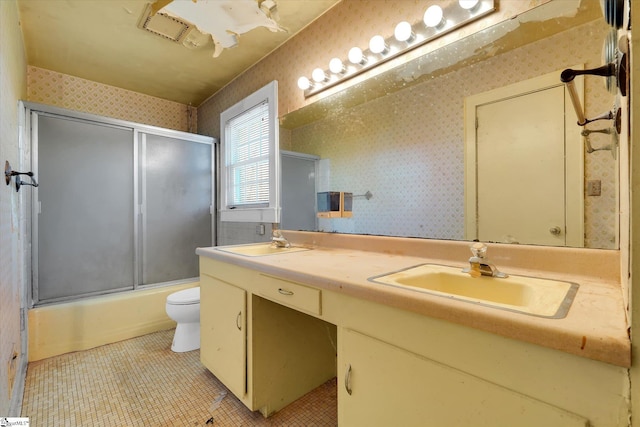 full bathroom featuring toilet, wallpapered walls, double vanity, and a sink